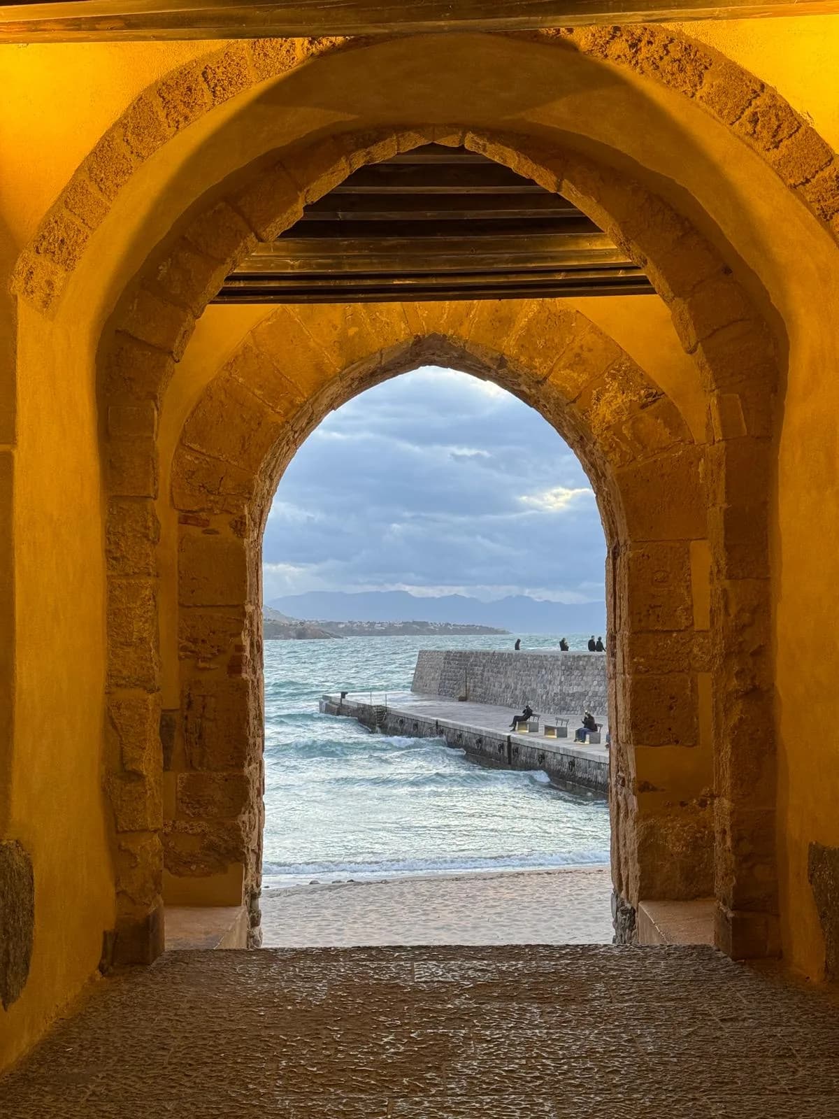 Stone arch framing the Cefalù seafront pier and marina