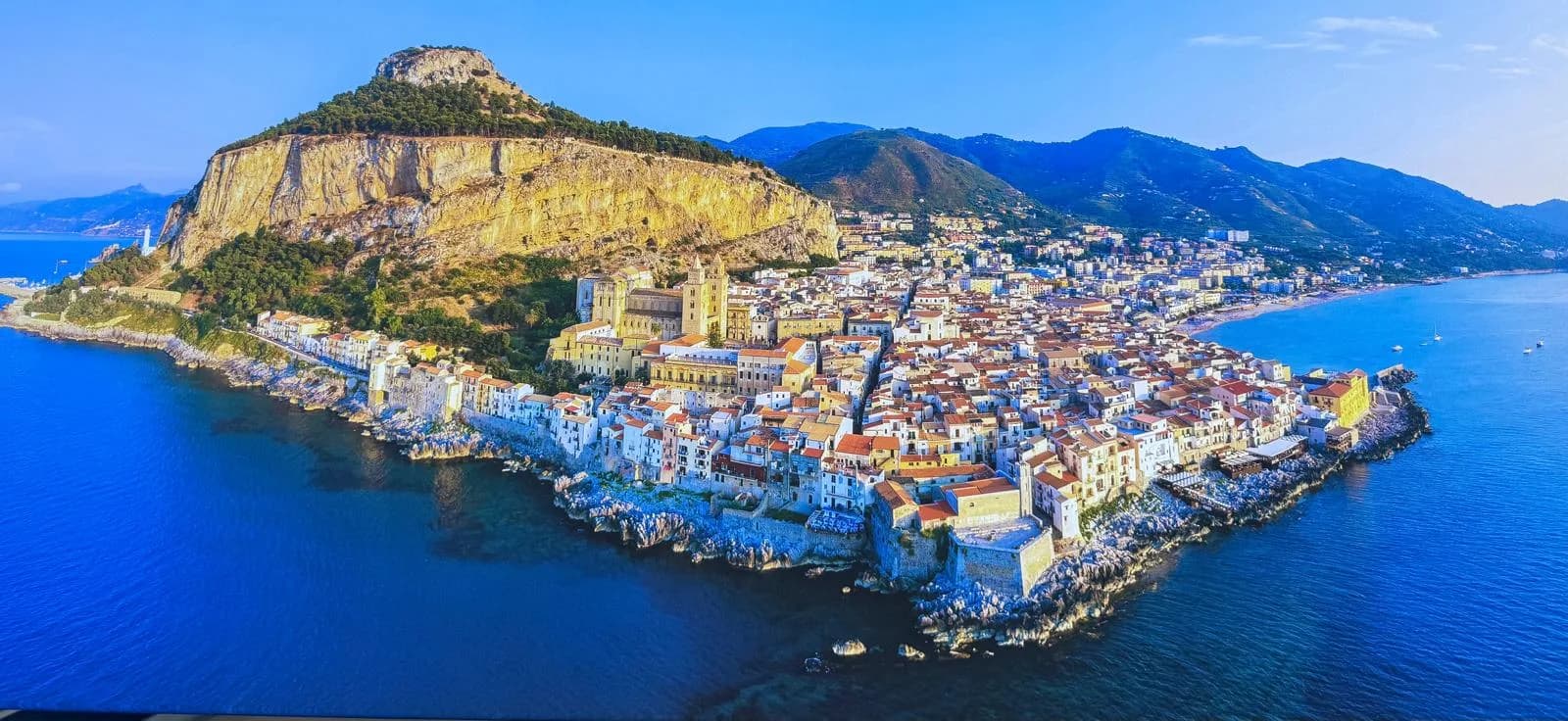 Aerial view of Cefalù headland, cathedral, and sandy beach curving along the Tyrrhenian coast