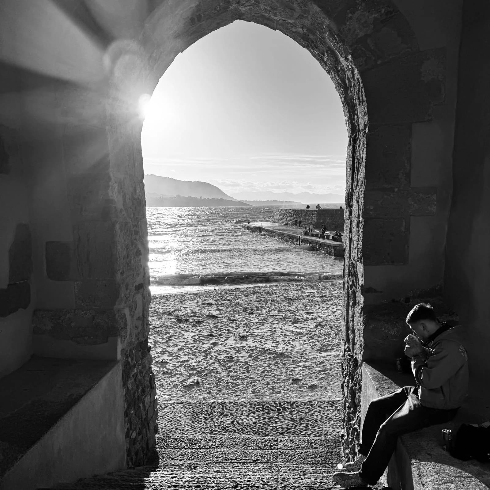 View of the sea and stone jetty framed by a medieval stone arch in Cefalù