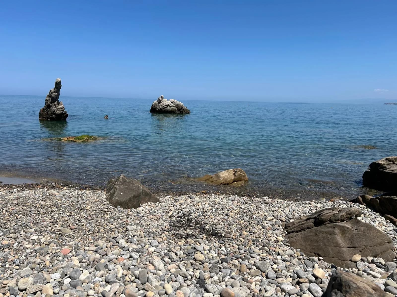 Pebble shore and clear turquoise water with rocks visible below the surface at Kalura, east of Cefalù