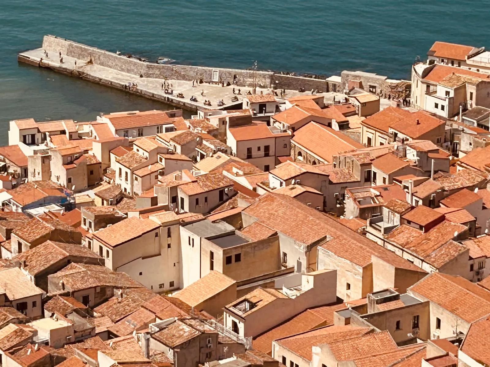 Aerial view of Cefalù harbour, rooftops, and the headland in golden light