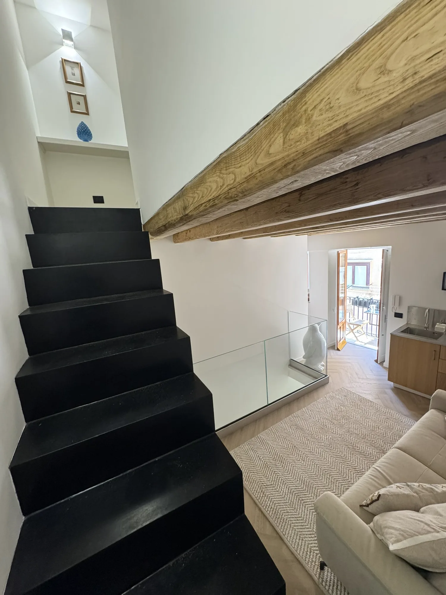 Sculptural black staircase rising beneath a restored timber beam