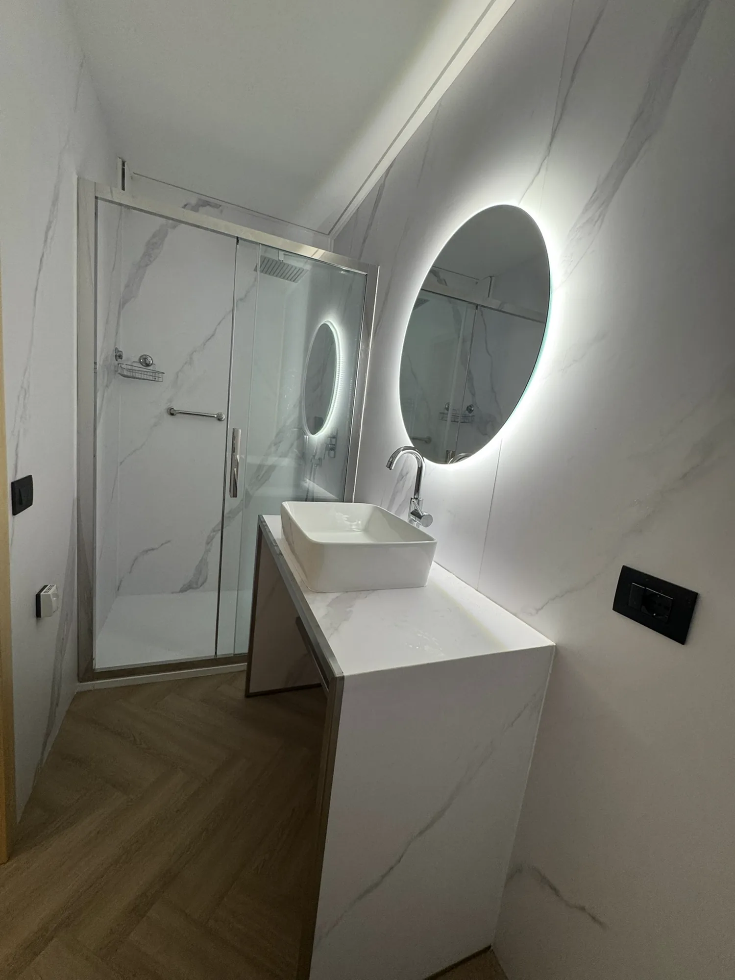 Marble bathroom with a walk-in rain shower and a backlit round mirror