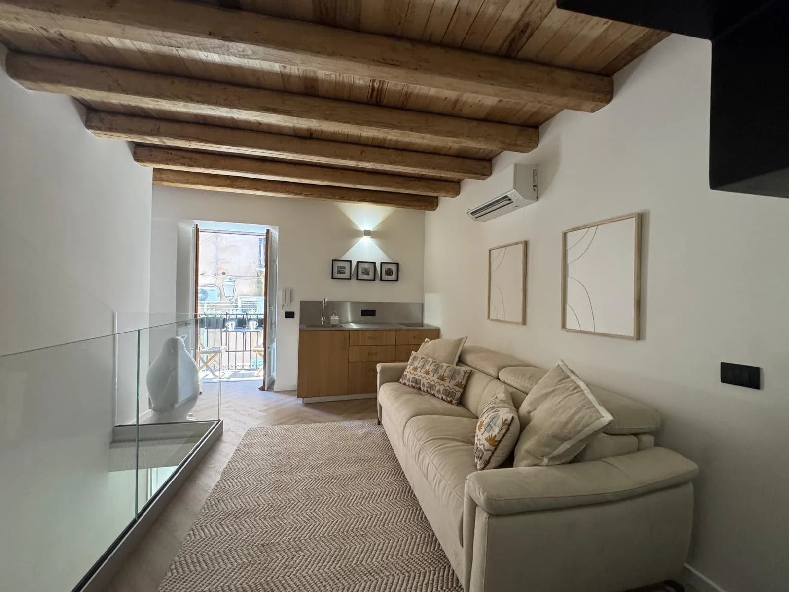 The mezzanine lounge at The Lavender Townhouse — a linen sofa under exposed timber beams, with a kitchenette and balcony beyond