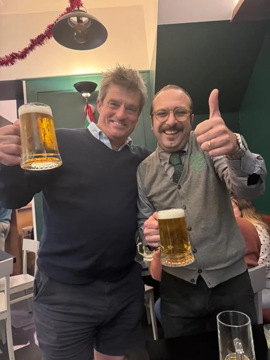 Two friends toasting with tall beer mugs at a bar in Cefalù