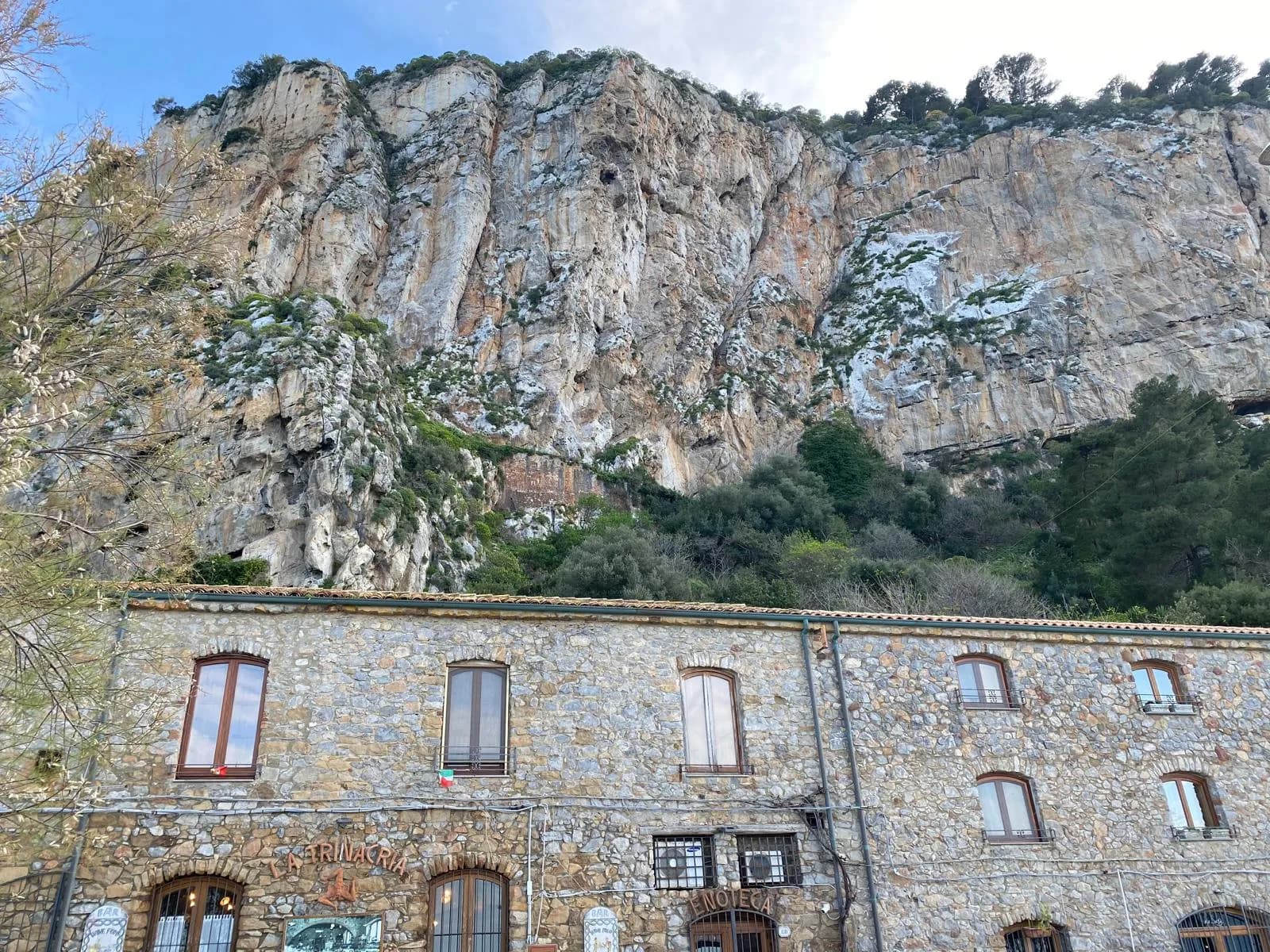 Stone building beneath the dramatic cliff face at the base of La Rocca