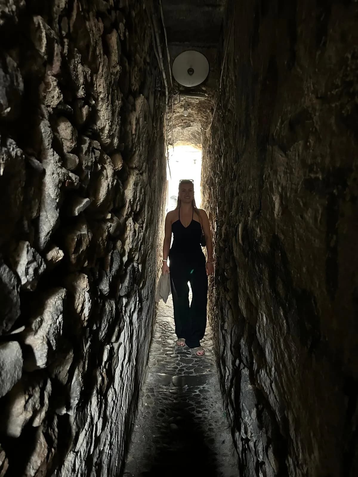 Woman walking through a narrow stone passage in Cefalù old town