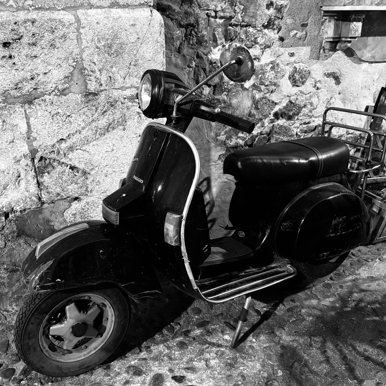 Vintage Vespa parked against a stone wall on a Sicilian coastal road